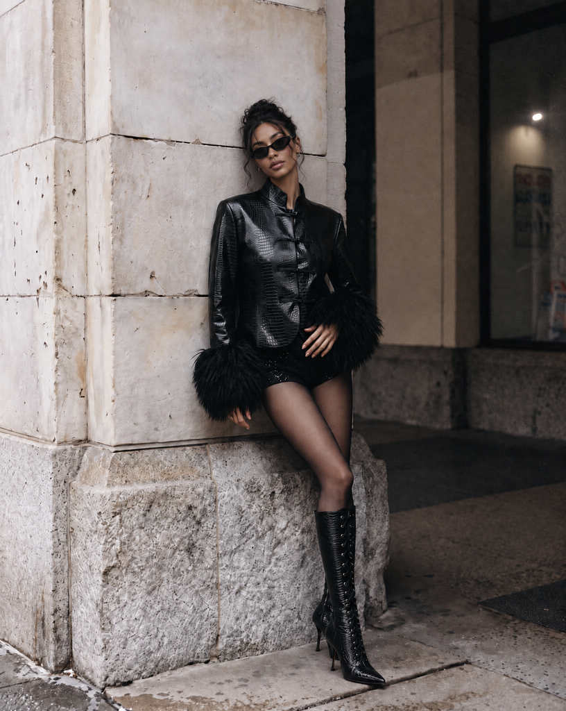 Model wearing NOIRÉ black croc-embossed faux leather jacket with oversized black faux fur cuffs and wide-leg denim jeans.